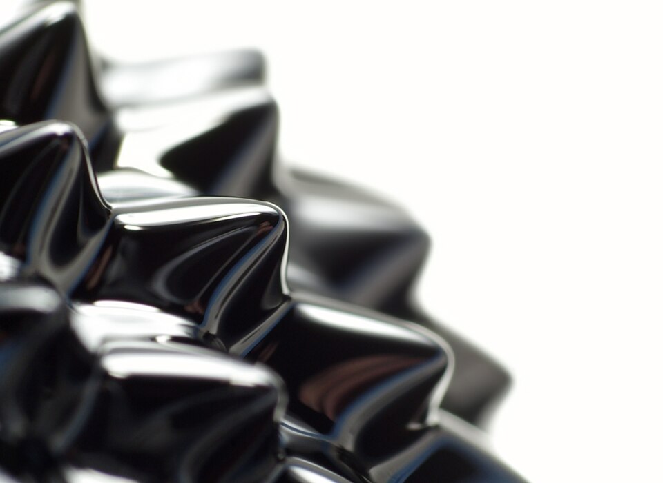 Ferrofluid drawn into sharp black spikes by a magnetic field, photographed close against white