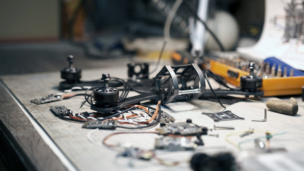 A drone frame mid-build on a cutting mat, surrounded by motors, flight controllers, wiring looms and hand tools