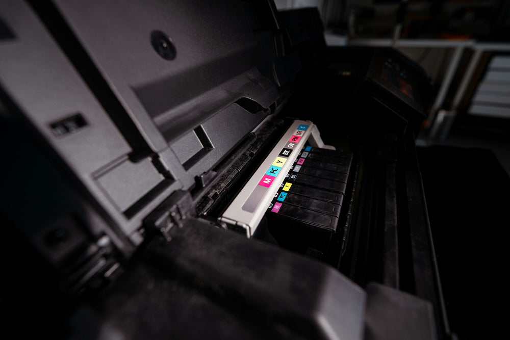 The open carriage of a wide-format printer, its labeled ink cartridges in a row